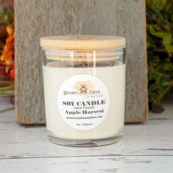 Brown's Creek Honey Farm Apple Harvest Soy Candle in a glass jar in front of a rustic piece of wood and rustic backdrop with harvest florals