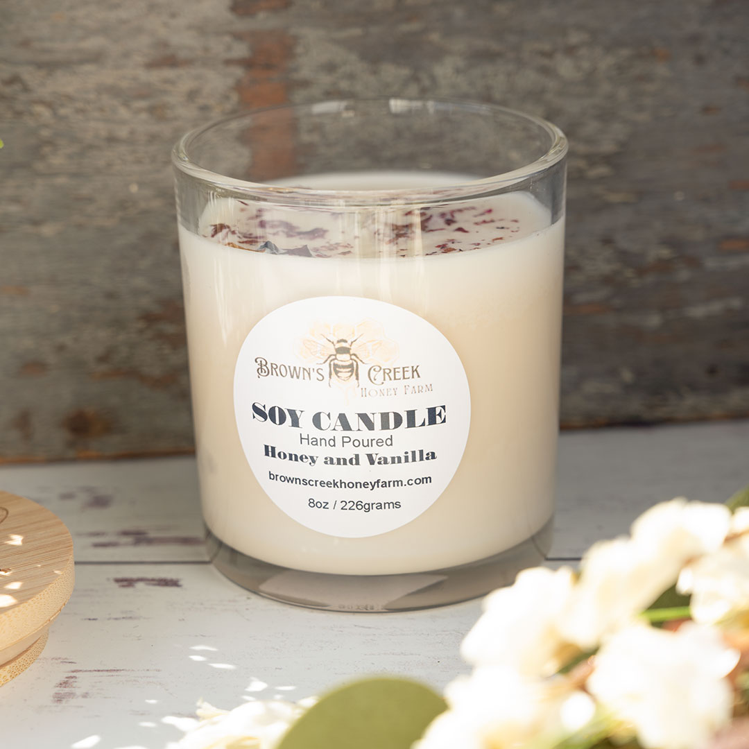 Open top view of the Brown's Creek Honey Farm Honey and Vanilla Soy Candle in a glass jar in front of a rustic piece of wood and rustic backdrop with harvest florals