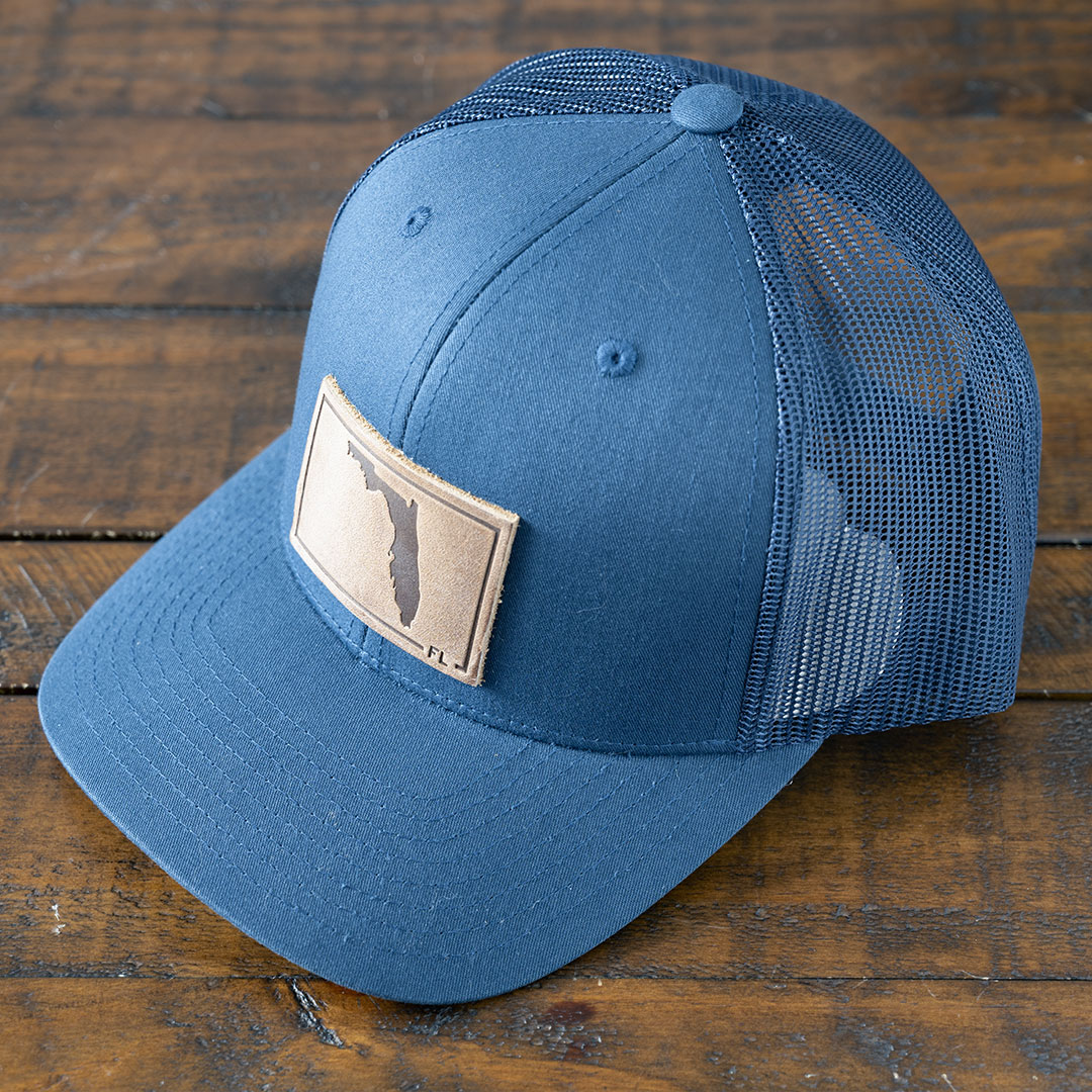 Angle view of the State of Florida leather patch hat in the color navy by RANGE Leather on a rustic wood tabletop