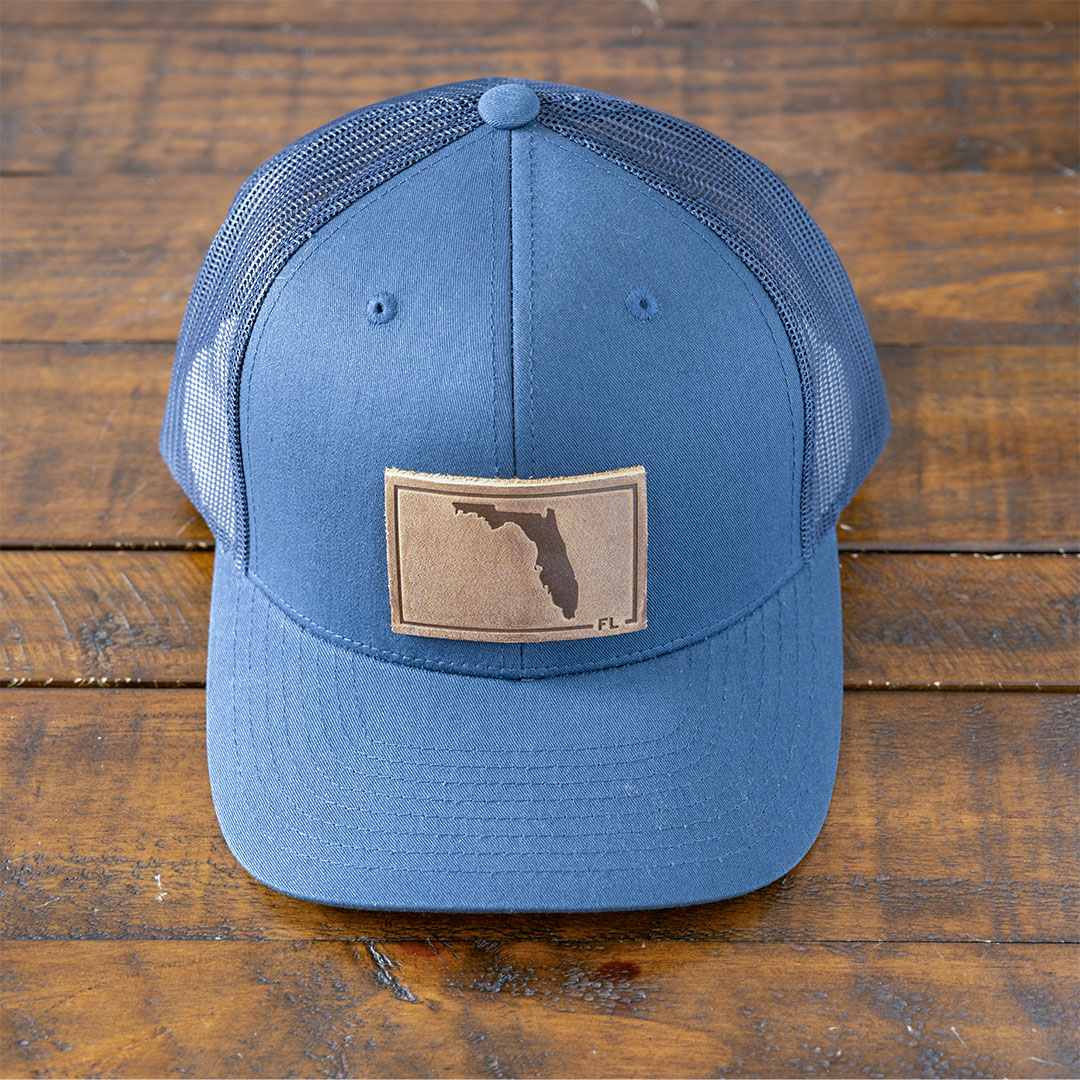 State of Florida leather patch hat in the color navy by RANGE Leather on a rustic wood tabletop