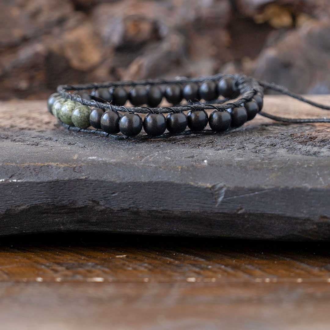 Side view of the men's Lotus & Luna Reef Keeper beaded bracelet resting on a piece of driftwood and rustic wood background
