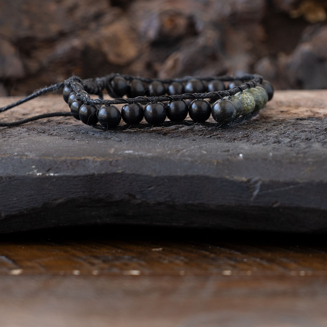Side view of the men's Lotus & Luna Reef Keeper beaded bracelet resting on a piece of driftwood and rustic wood background