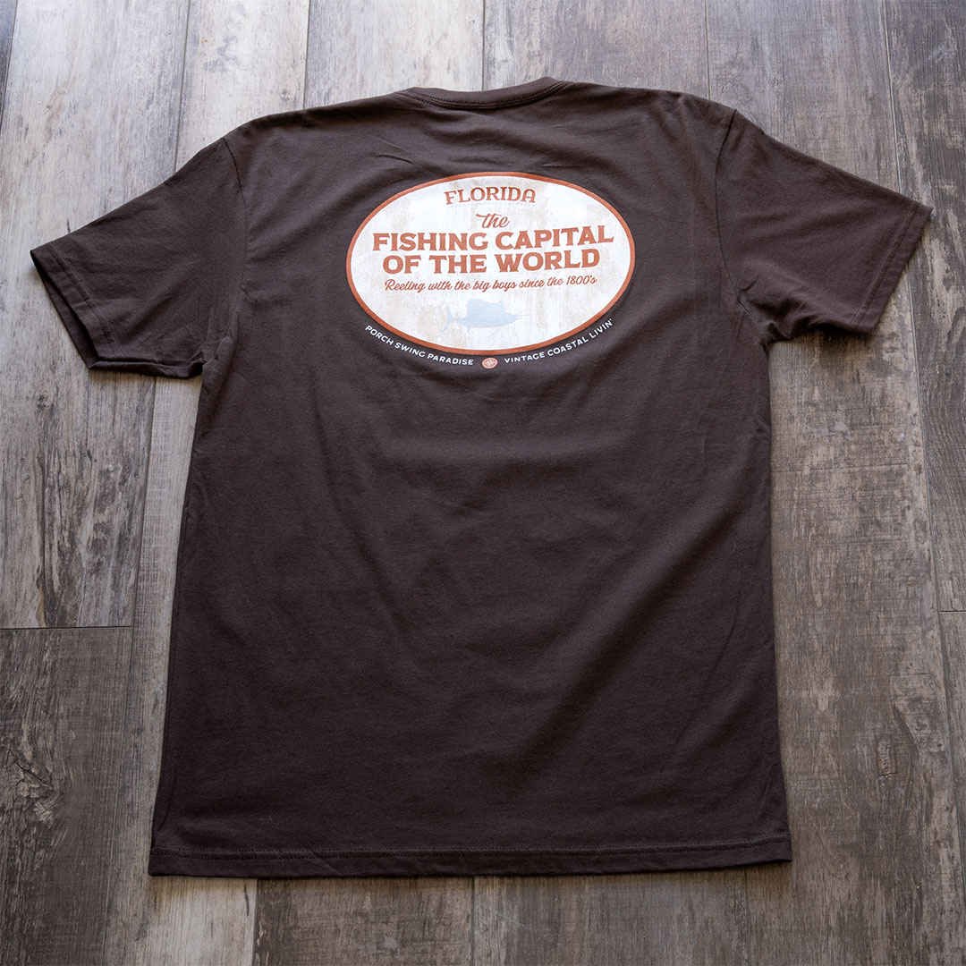 Full back view of the Porch Swing paradise Graphic Tee Florida... The Fishing Capital of the World graphic tee in the color chocolate against a rustic backdrop