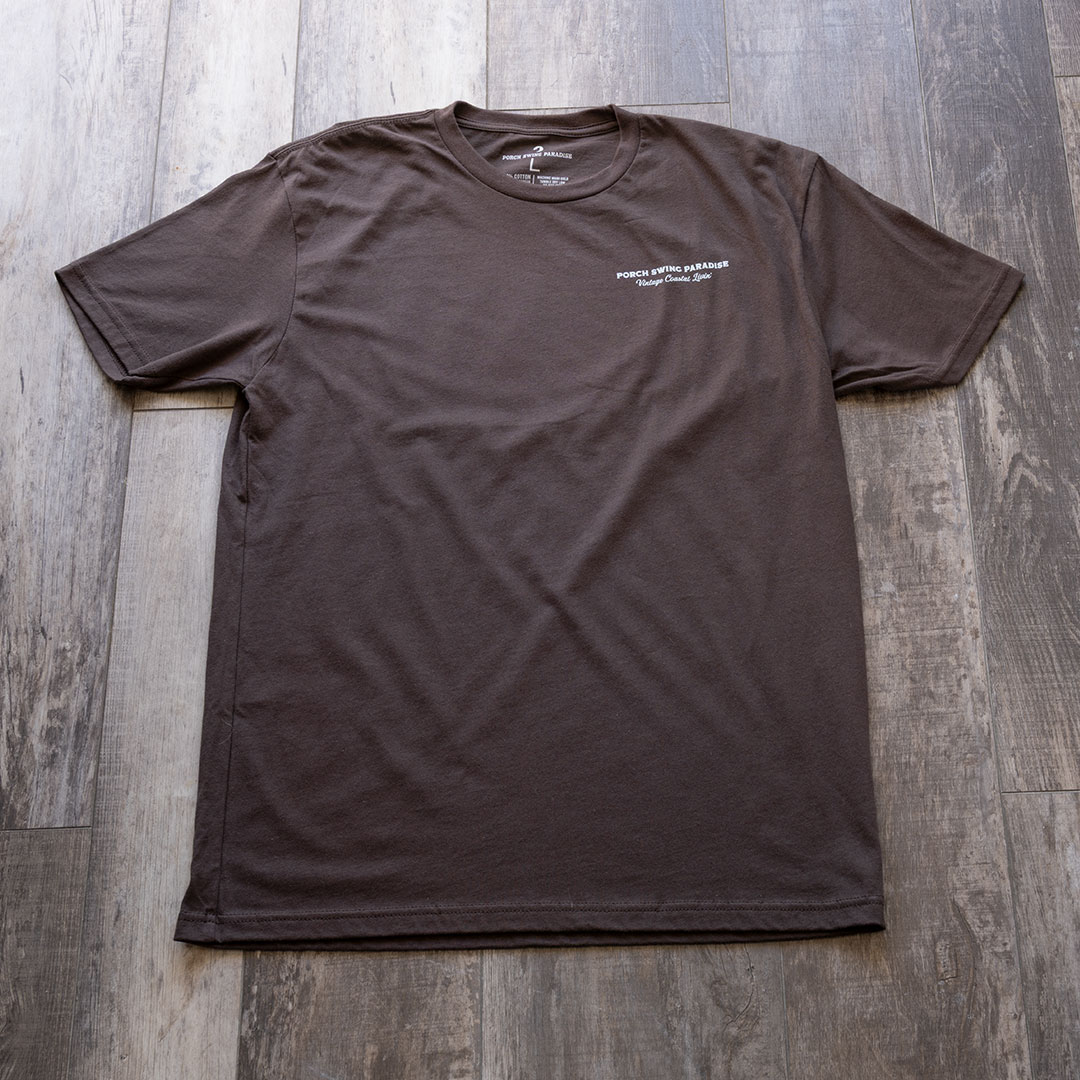 Full front view of the Porch Swing paradise Graphic Tee Florida... The Fishing Capital of the World graphic tee in the color chocolate against a rustic backdrop