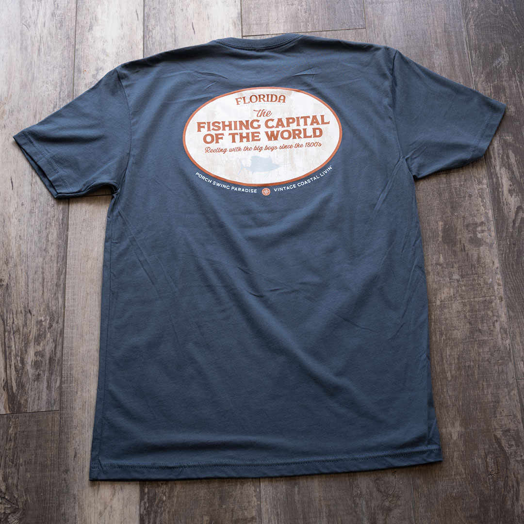 Full back view of the Porch Swing paradise Graphic Tee Florida... The Fishing Capital of the World graphic tee in the color indigo against a rustic backdrop