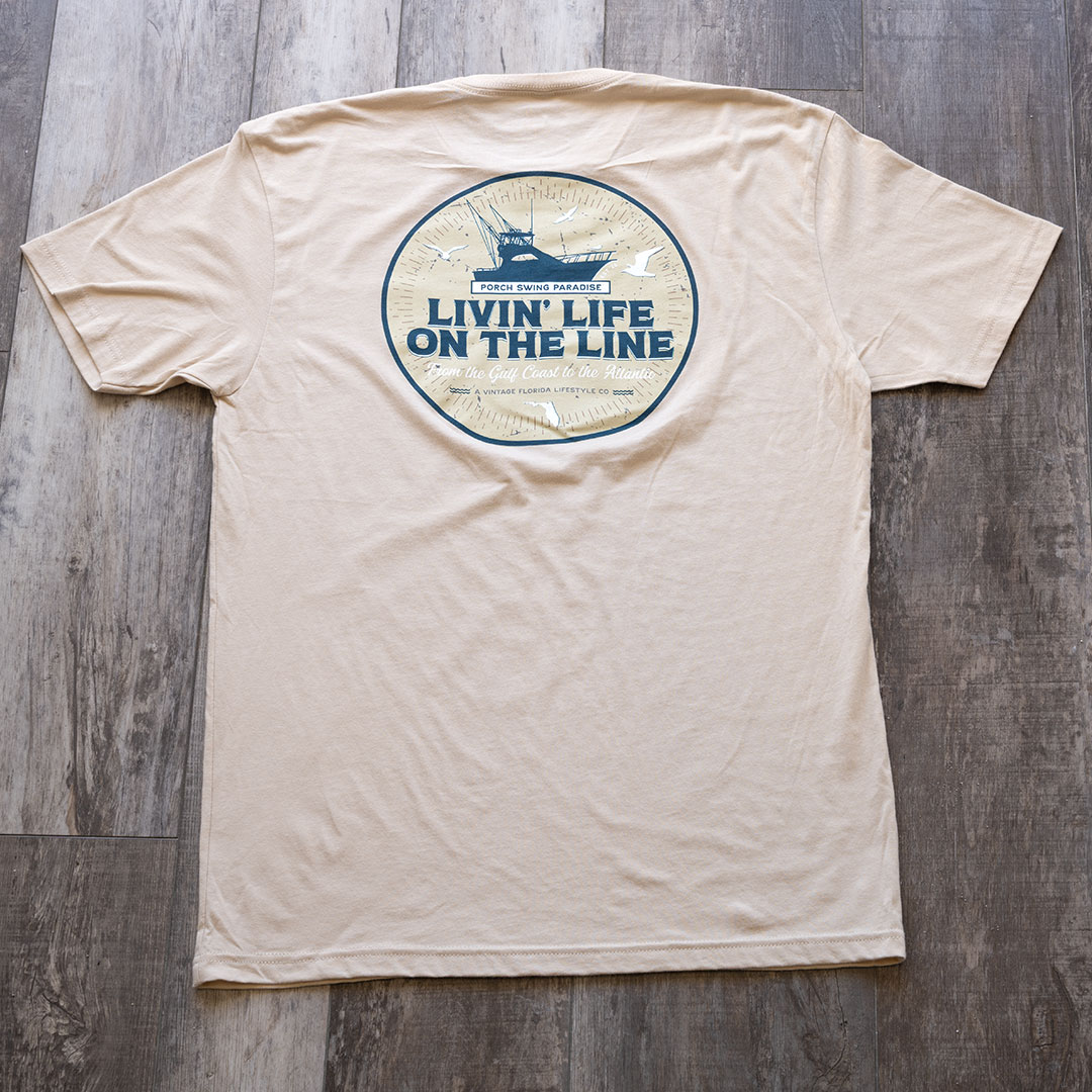 Full back view of the back graphic on the Livin' Life on the Line tee in the color cream by Porch Swing Paradise on a rustic wood backdrop