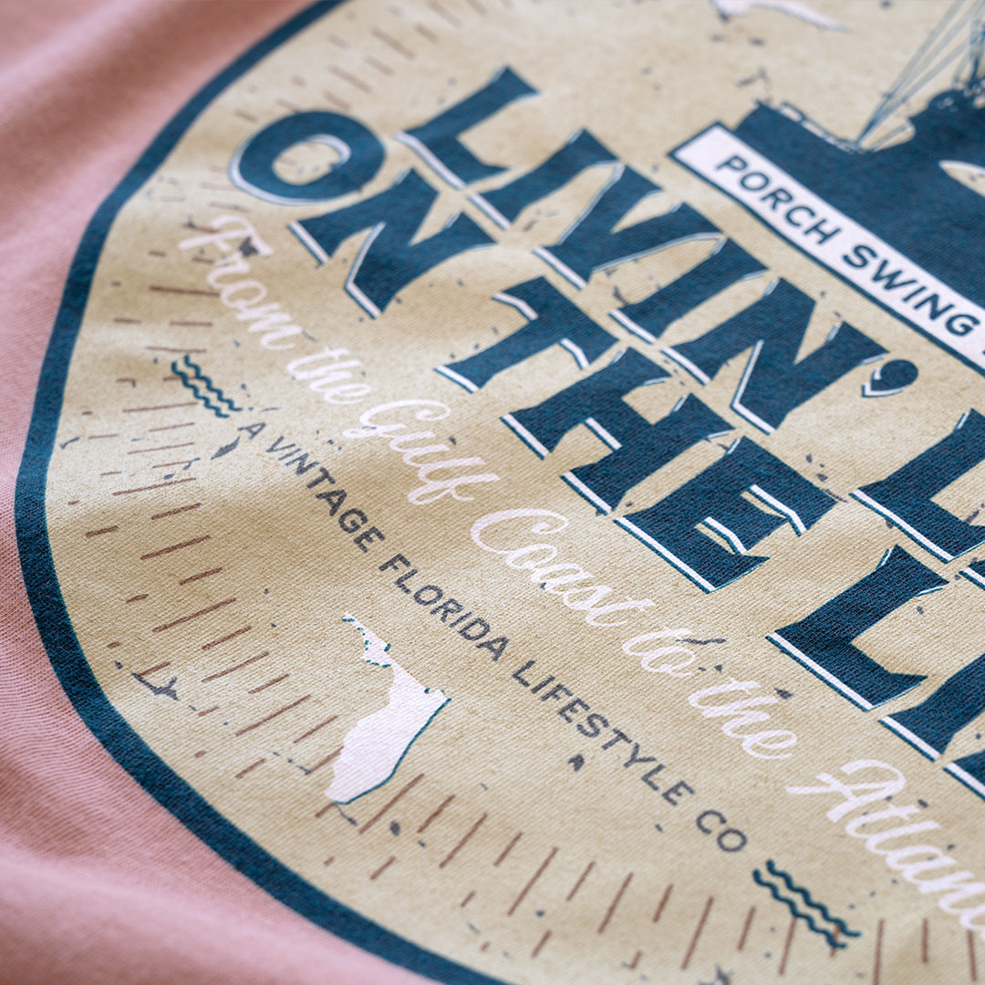 Top closeup view of the back graphic on the Livin' Life on the Line tee in the color dessert pink by Porch Swing Paradise
