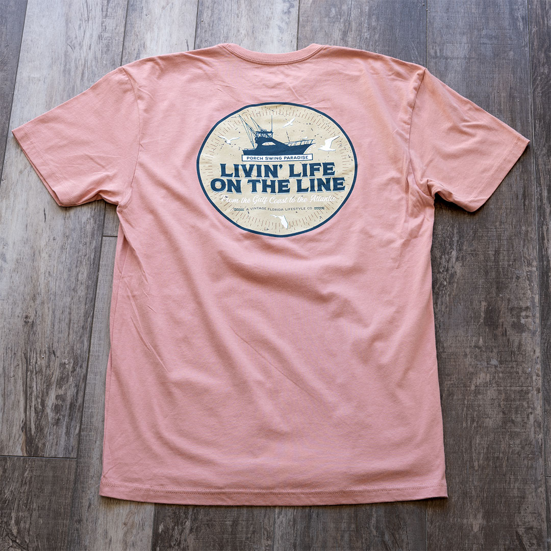 Full back view of the back graphic on the Livin' Life on the Line tee in the color dessert pink by Porch Swing Paradise on a rustic wood backdrop