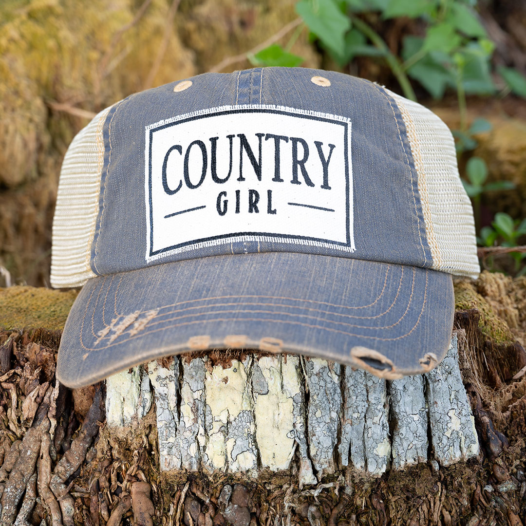 Country Girl distressed trucker cap in navy by Vintage Life sitting on a tree stump
