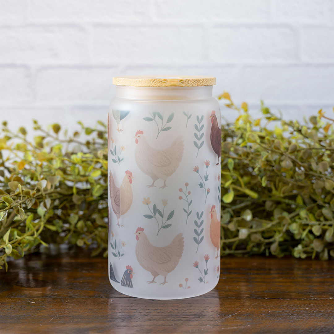 The Colorful Chickens glass tumbler by Emma K Designs in front of greenery and against a rustic wood background