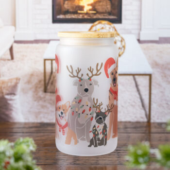 The Dogs of Christmas frosted glass tumbler by Emma K Designs sitting on a rustic tabletop in front of a wintery home backdrop