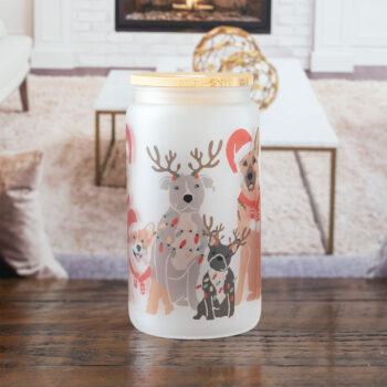 The Dogs of Christmas frosted glass tumbler by Emma K Designs sitting on a rustic tabletop in front of a wintery home backdrop