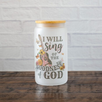 I Will Sing of the Goodness of the Lord glass tumbler by Emma K Designs against a white and a dark wood background