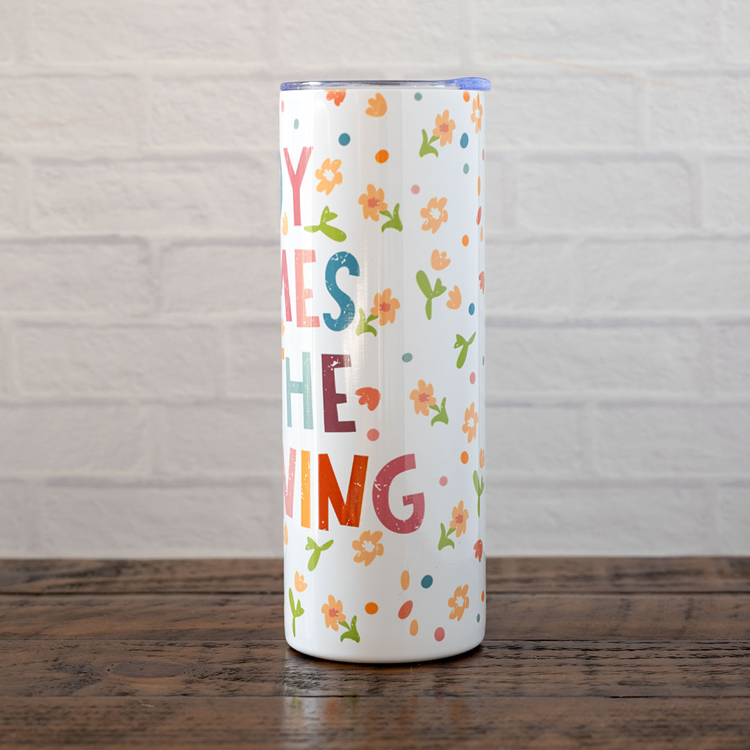 Side view of the Joy Comes in the Morning stainless skinny tumbler against rustic wood backdrop