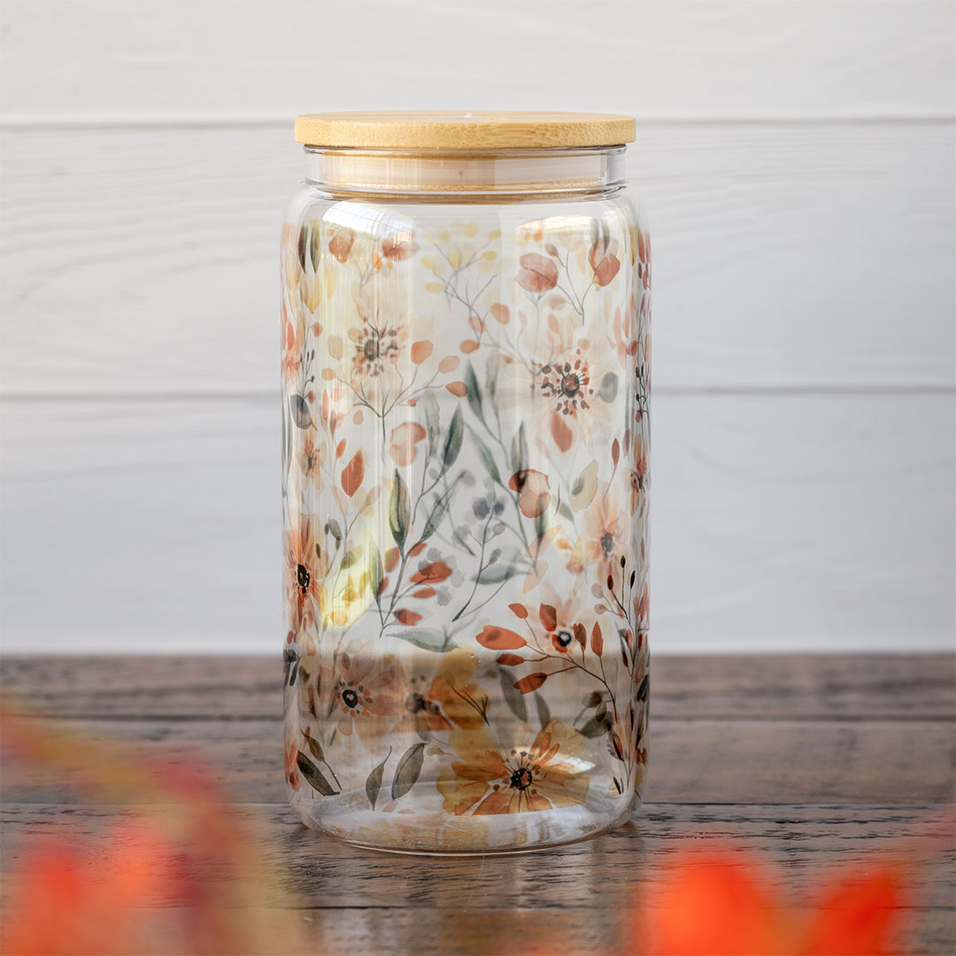 Angle view of the Emma K Designs The Meadows glass tumbler in front of greenery and against a rustic wooden backdrop