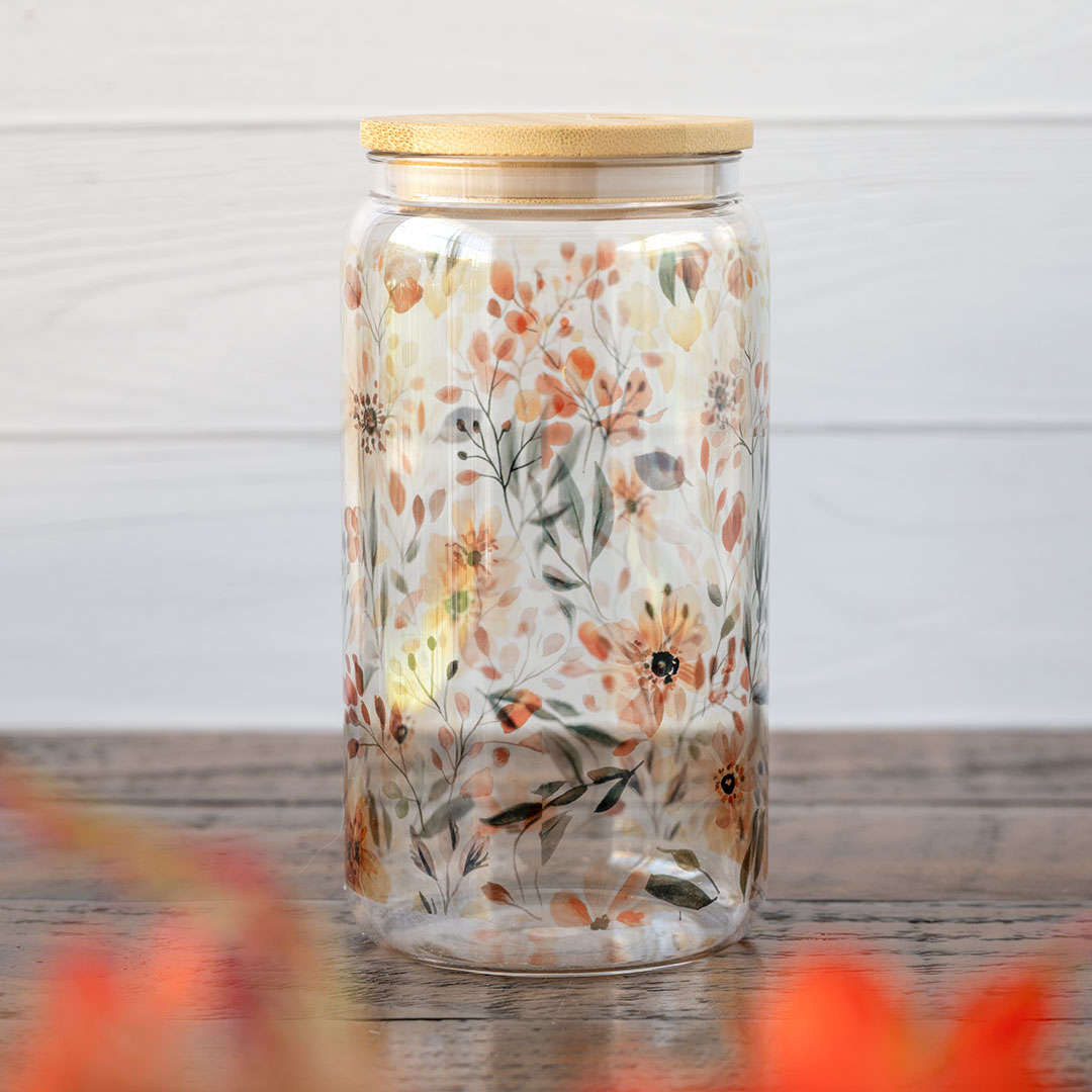 The Emma K Designs The Meadows glass tumbler in front of greenery and against a rustic wooden backdrop