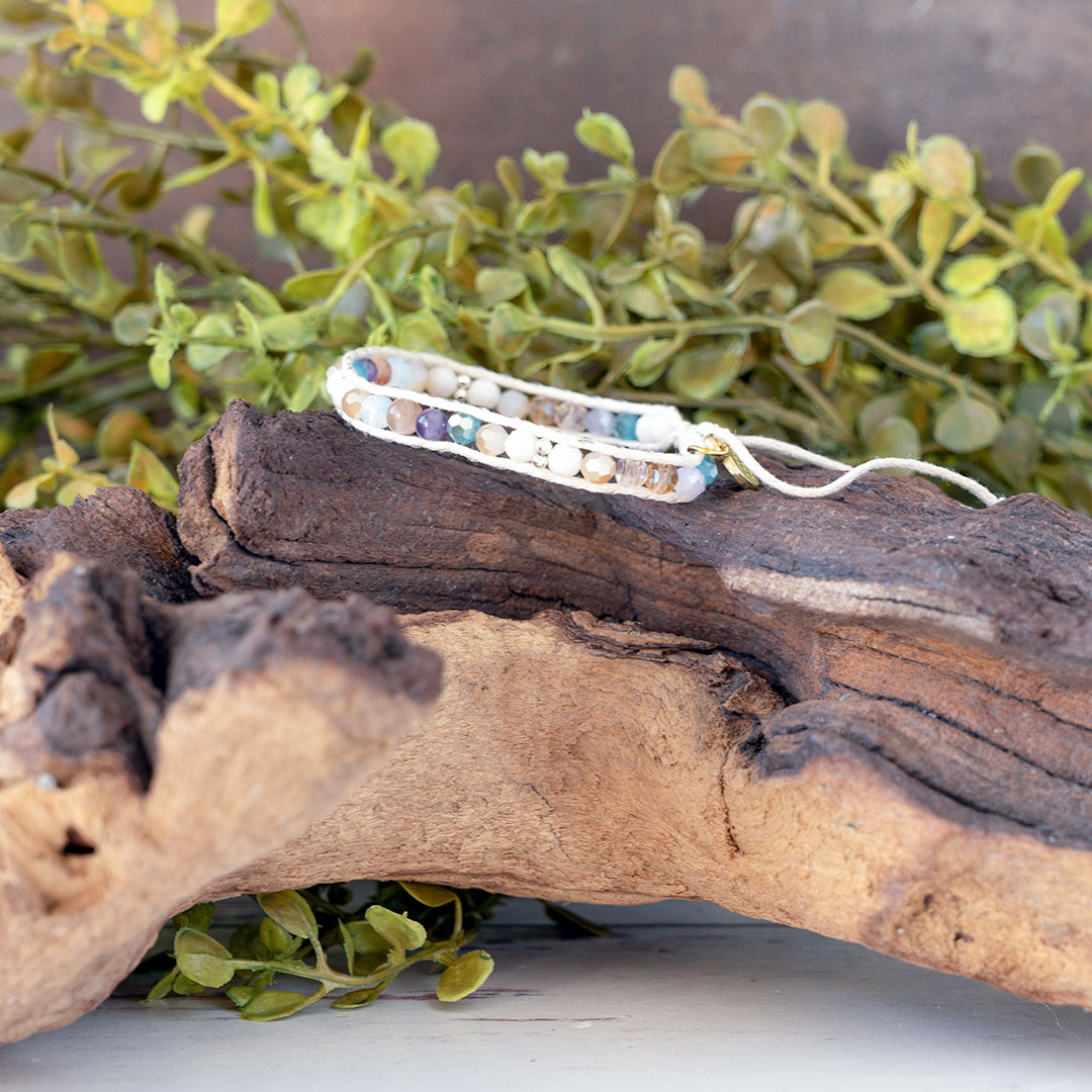 The Coastal Sunset side view of the Moonbeam Bracelet on a piece of driftwood with a rustic backdrop