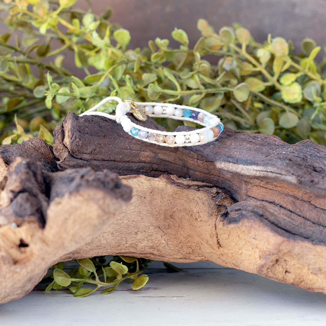 The Coastal Sunset side view of the Moonbeam Bracelet on a piece of driftwood with a rustic backdrop