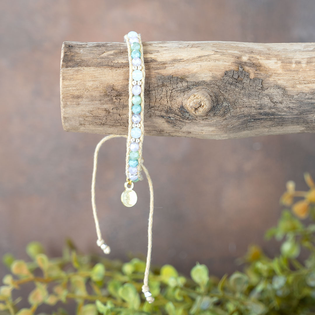 The Natural Wonder Moonbeam Bracelet dangling on a piece of driftwood with a rustic backdrop