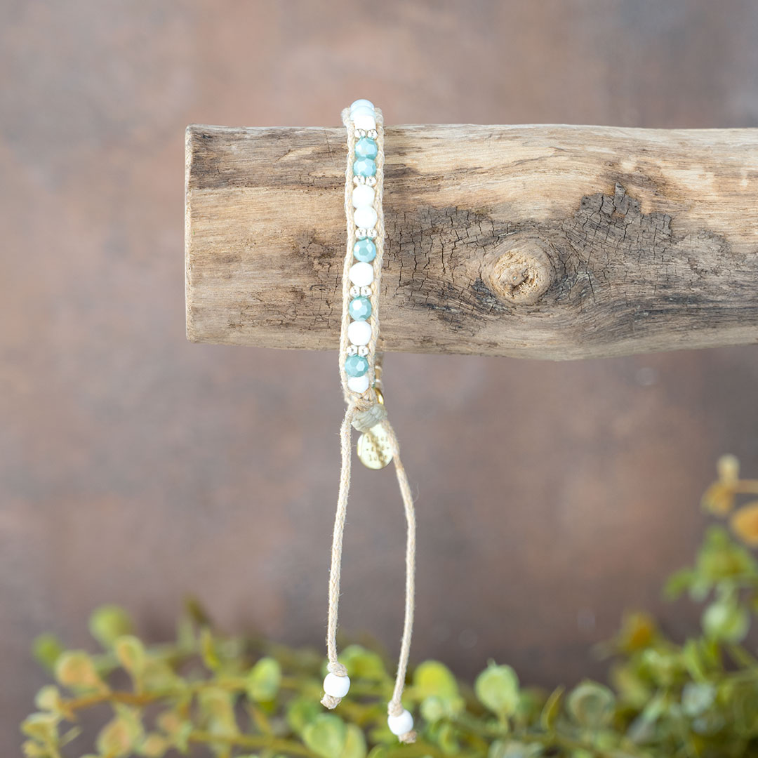 The Pristine Beaches Moonbeam Bracelet dangling on a piece of driftwood with a rustic backdrop