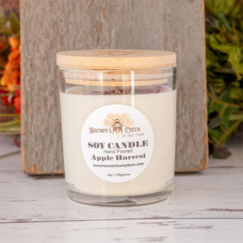 Brown's Creek Honey Farm Apple Harvest Soy Candle in a glass jar in front of a rustic piece of wood and rustic backdrop with harvest florals