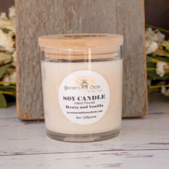 Brown's Creek Honey Farm Honey and Vanilla Soy Candle in a glass jar in front of a rustic piece of wood and rustic backdrop with harvest florals