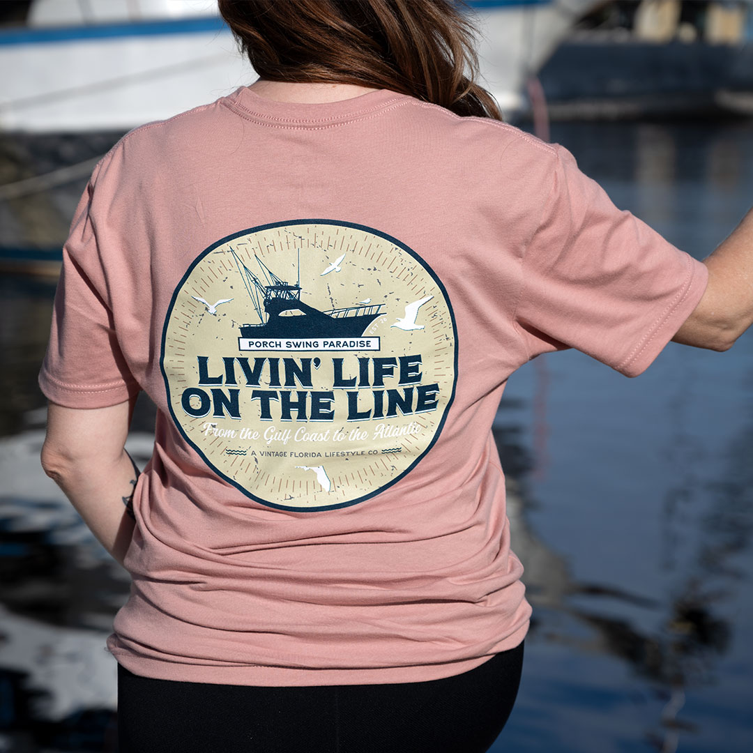 Full back view of the Livin' Life on the Line tee in the color dessert pink by Porch Swing Paradise being worn by Kim at a fishing village in Tarpon Springs, FL